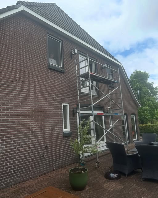 Steiger tegen een bakstenen woning voor het buitenschilderwerk van kozijnen en dakrand