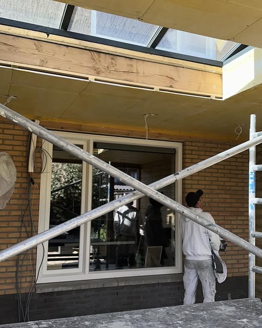 Schilder van Klement schildert witte kozijnen onder een overkapping met glazen dak